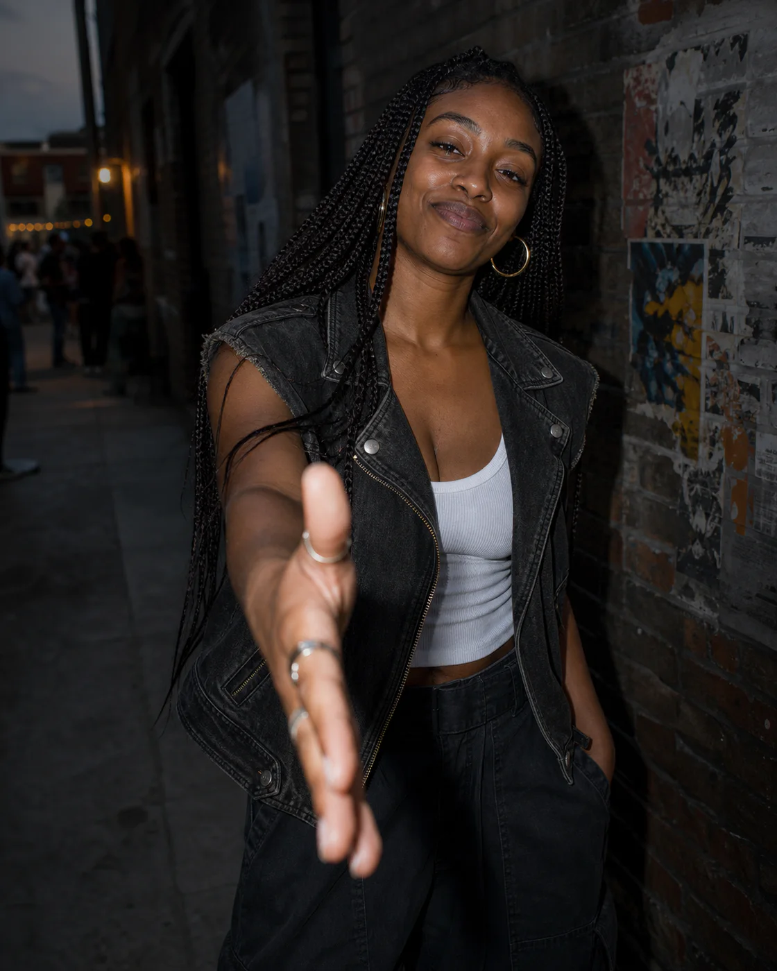 Nia Brooks in washed black denim in a brick alley, reaching forward to offer a dap.